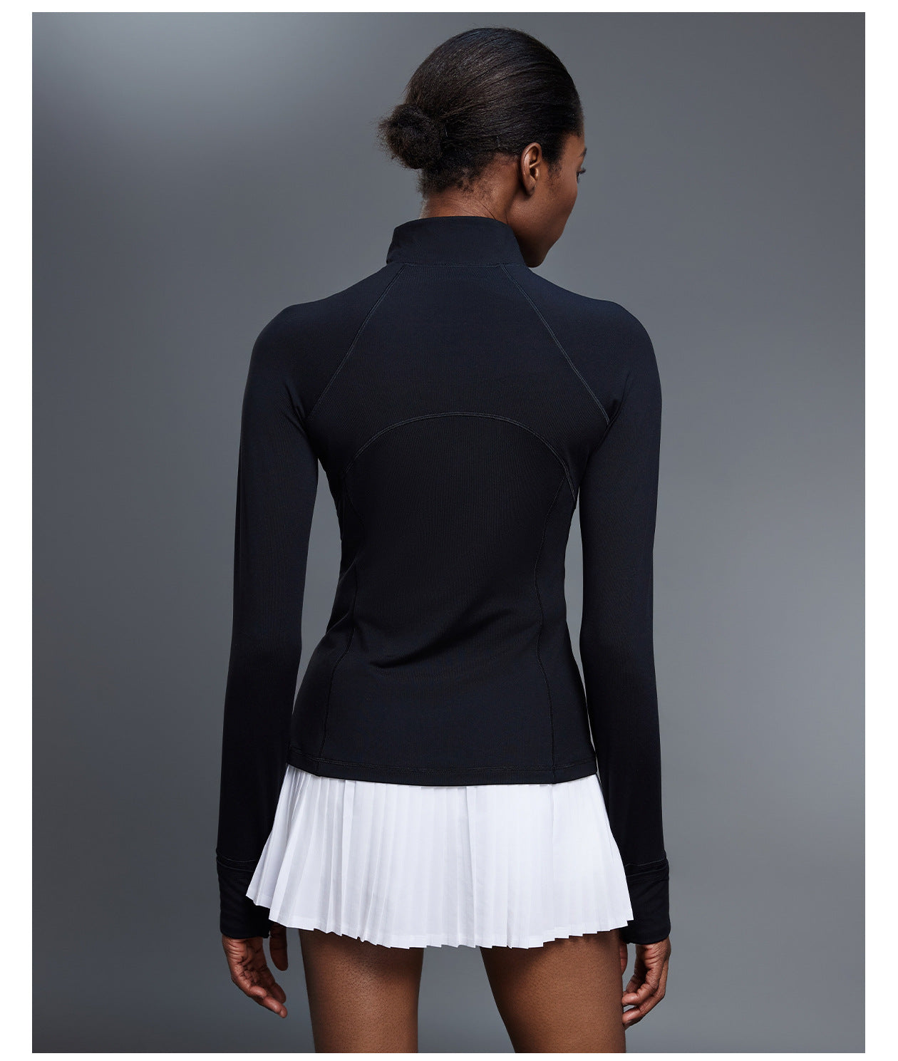 Back view of black quarter-zip golf pullover with a white pleated skirt, showing the curved back seams