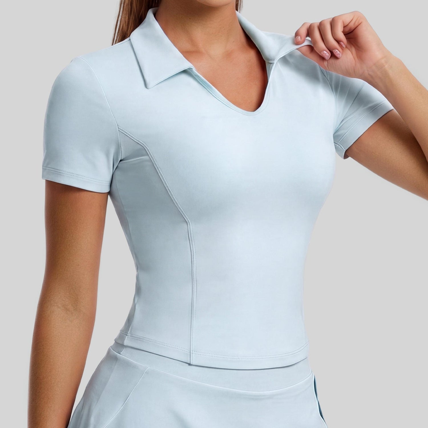 Light blue open collar golf polo with a matching flared skirt, front view while adjusting the collar