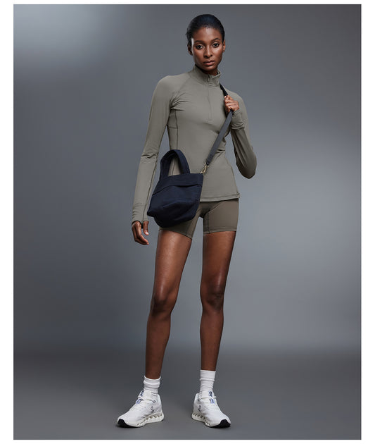 Olive quarter-zip golf pullover with matching shorts, front view holding the strap of a navy crossbody bag