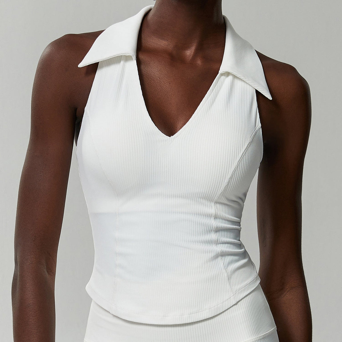 White ribbed sleeveless golf top on a model, front view showing the ribbed knit and curved hem