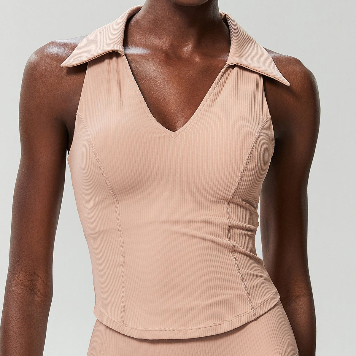 Beige ribbed sleeveless golf top on a model, front view showing the ribbed knit and curved hem