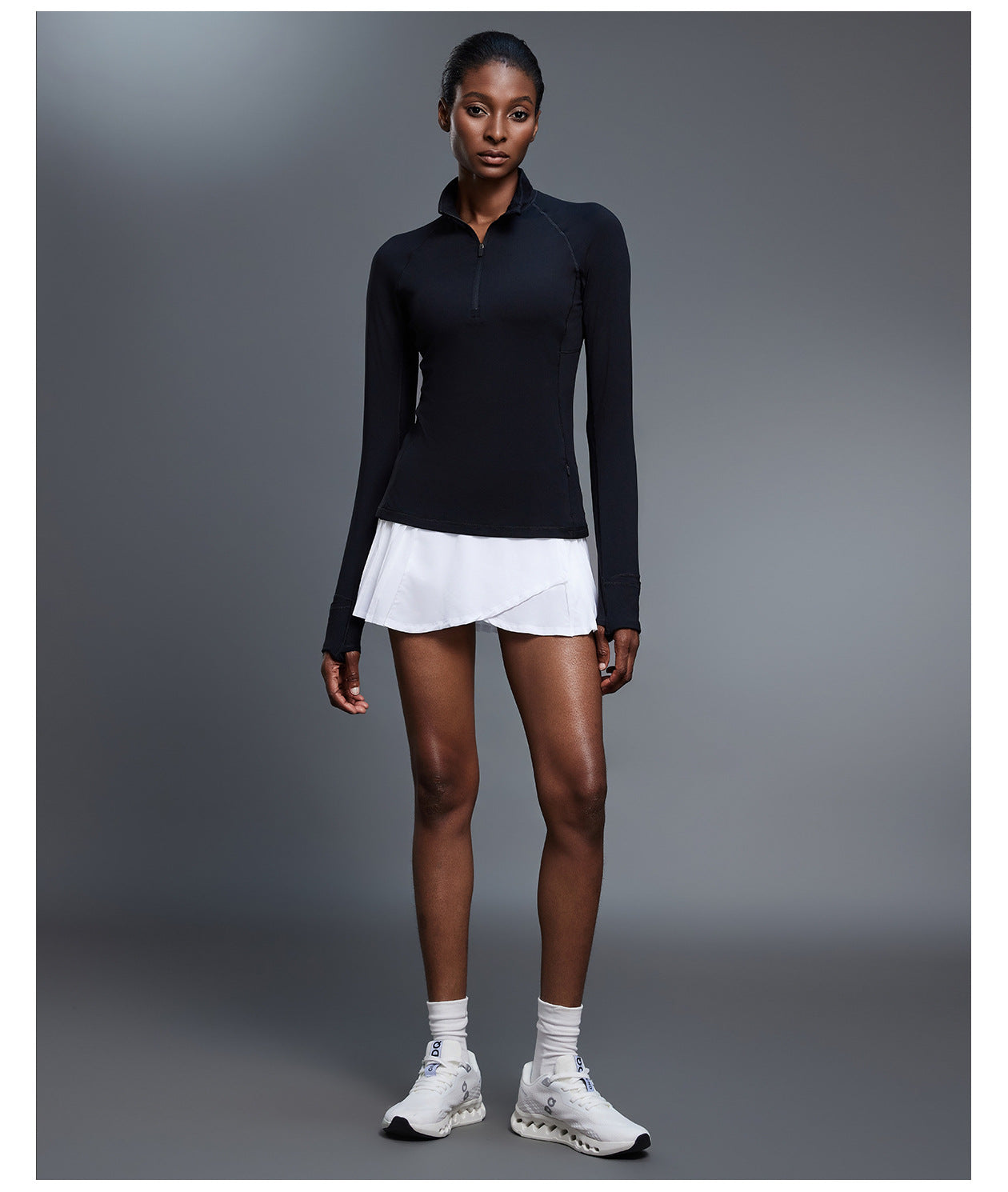 Black quarter-zip golf pullover with a white pleated skirt, full-length front view showing the side zip pocket
