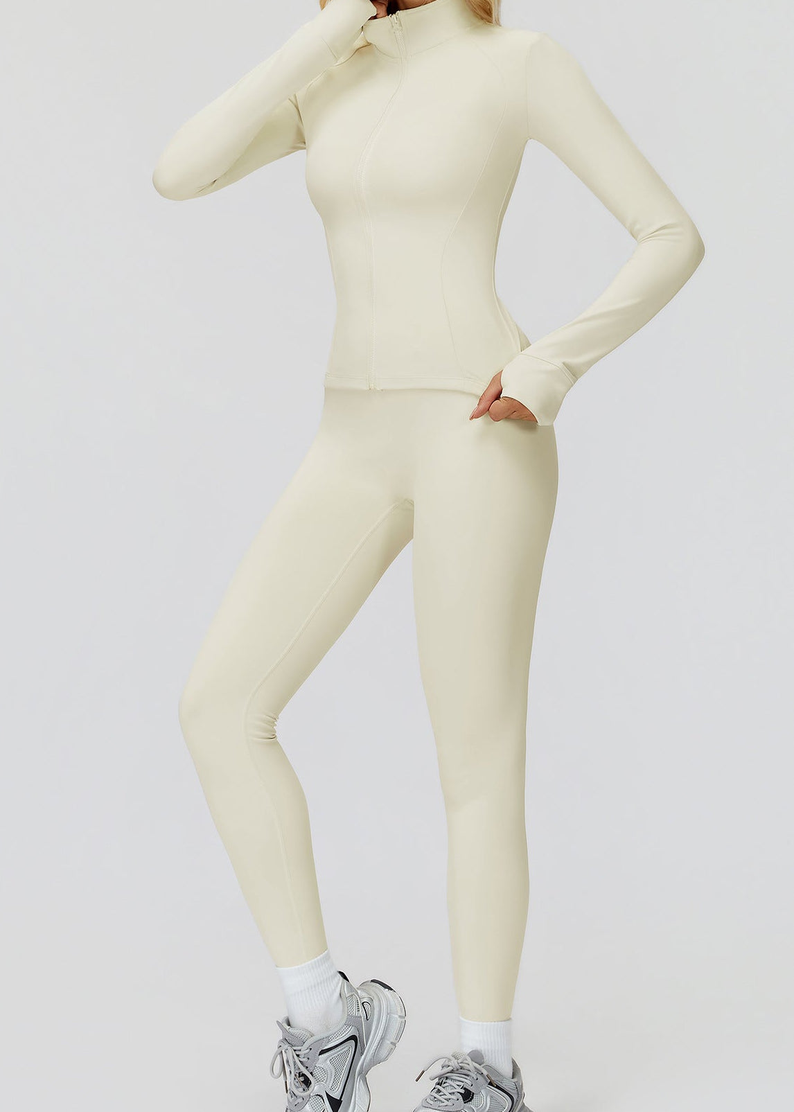 Cream full-zip jacket zipped up with matching leggings, full-length front view with one hand at the collar