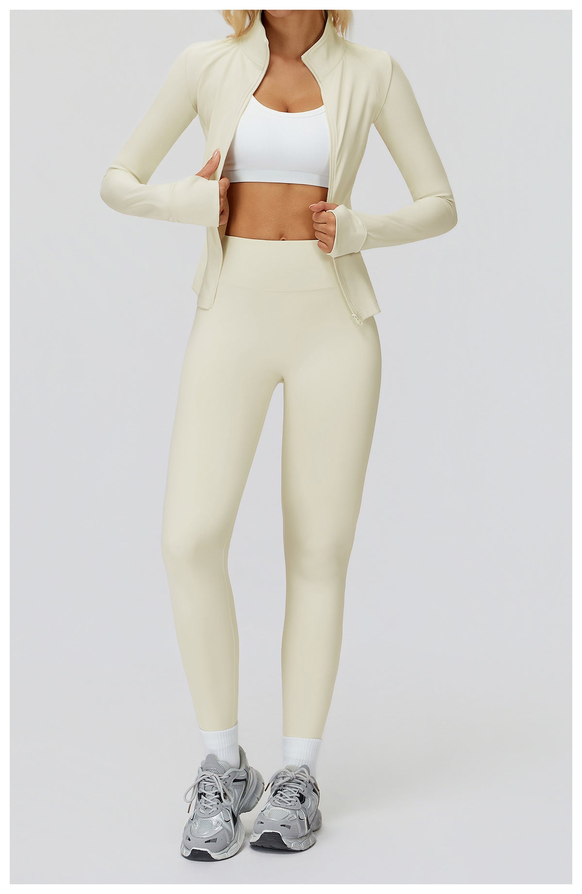 Cream stand collar golf jacket worn open over a white sports bra, full-length view with hands on the zip