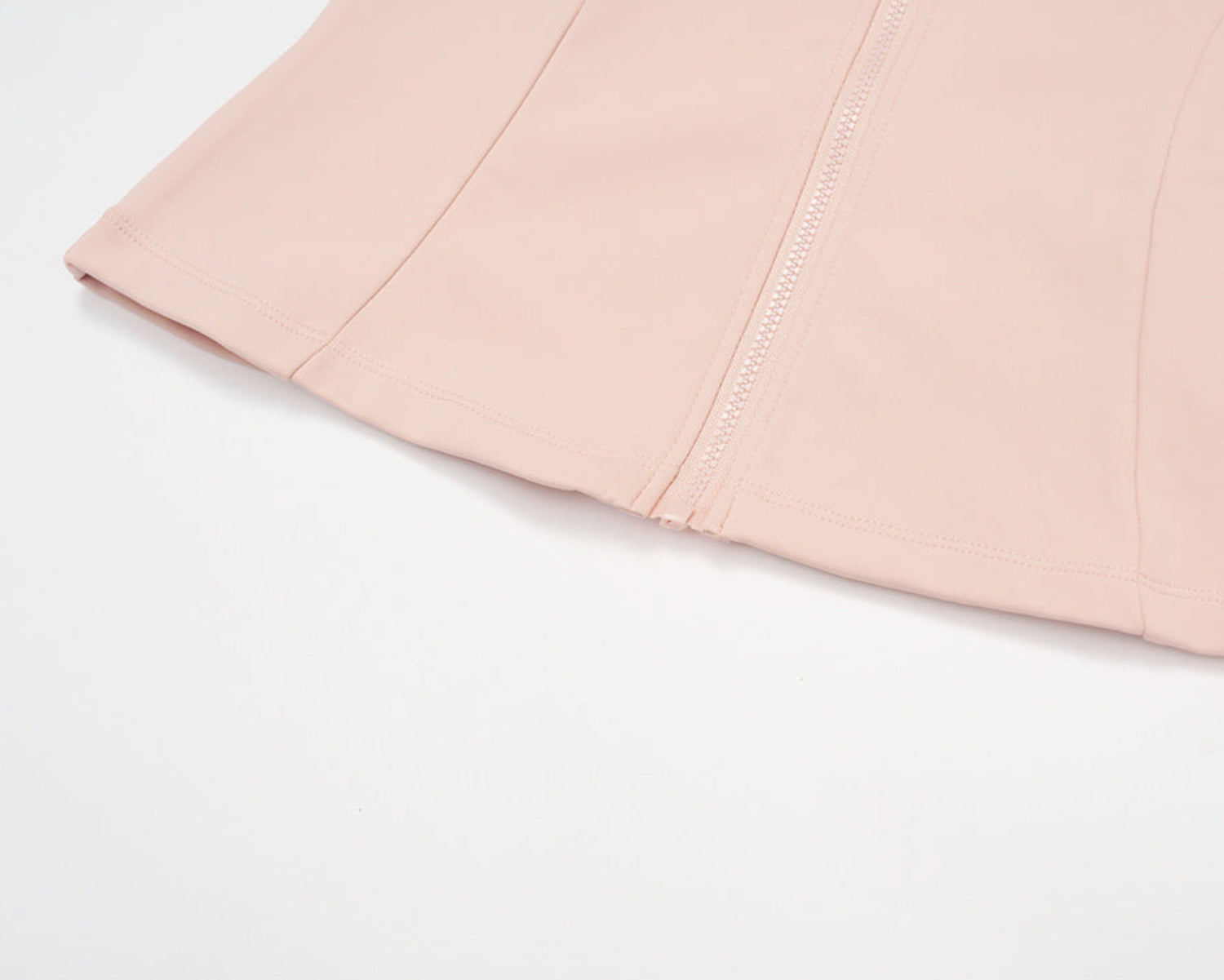 Close-up of the pink golf jacket hem, showing the zip end and stitched front panel seams, laid flat